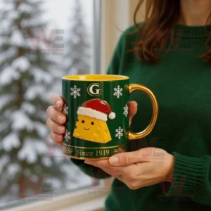 A person holding a green and yellow holiday mug with a smiling cheese wedge and Santa hat design!