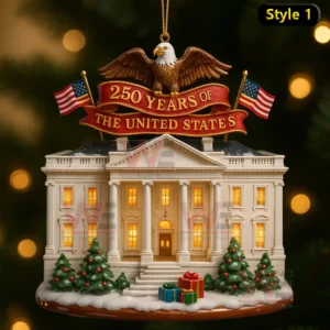 A festive ornament of a white building with lit windows snowy decorations trees gifts and an eagle holding a celebratory banner!