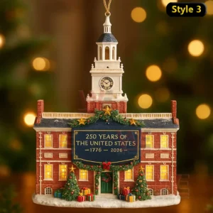 A festive brick building ornament with a clock tower glowing windows holiday greenery trees gifts and a banner marking two hundred fifty years of the United States!