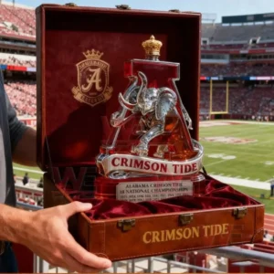 Alabama Crimson Tide National Champions Whiskey Bottle 8 The image features an Alabama Crimson Tide bottle placed on a wooden table surrounded by sports decor including helmets and framed jerseys!