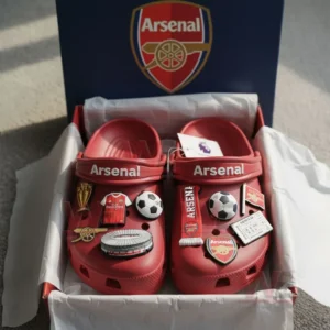 Red Arsenal Crocs with football-related charms displayed inside an Arsenal-themed box.