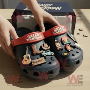 Bailey Zimmerman Crocs Clogs with Charms 8 Bailey Zimmerman Crocs being lifted from packaging by hands showing detailed charms under warm light on a wooden background!