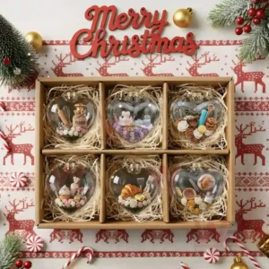 Alt text: A collection of six heart-shaped glass ornaments with different miniature bakery scenes, packaged for Christmas.