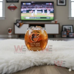 A Baltimore Orioles anniversary whiskey glass with ice on a white rug in front of a television showing a baseball game.