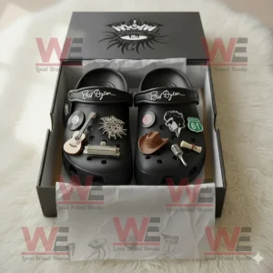 Black Crocs with Bob Dylan signature and music inspired charms arranged in an open box with detailed packaging design on a soft white surface!