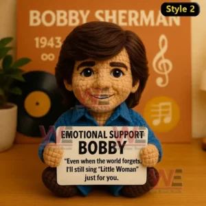 A crochet doll with brown hair and blue clothes sitting by a record backdrop holding an emotional support sign with a musical message!