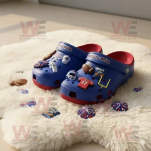 Blue and red Buffalo Bills Crocs with miniature football accessories sitting on a soft white rug.