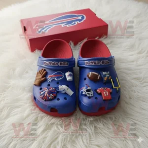 Blue and red Buffalo Bills Crocs with football charms and logo placed on white furry surface near a matching red box.