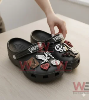 Black decorated clogs on a wooden table with various raised music themed charms.