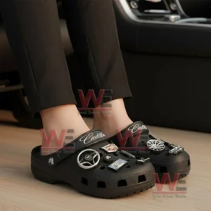 A pair of black clogs on feet featuring multiple Cadillac related decorative charms!
