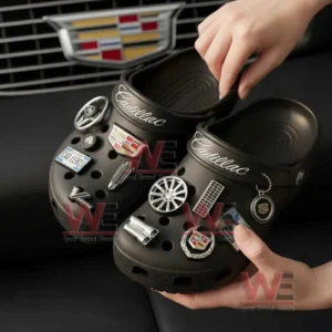 A pair of black clogs being held up displaying numerous Cadillac themed decorative charms!