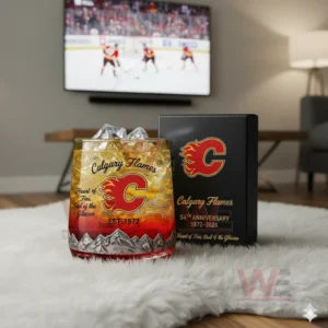 A Calgary Flames anniversary whiskey glass with ice on a white rug in front of a television showing a hockey game.