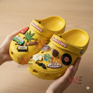 A pair of charm decorated yellow clogs being held by hands above a wooden surface.