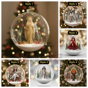 A clear glass ornament containing a woman in a shimmering gold gown with snowy trees and gifts inside against a blurred Christmas light background!