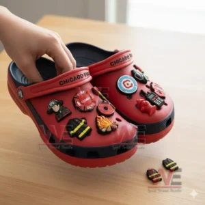 Red firefighter themed clogs with multiple charms being touched by a hand on a wooden surface!