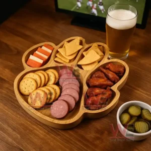 A paw shaped wooden tray filled with snacks sits on a wooden table beside a glass of beer with a sports scene showing on a screen behind it!