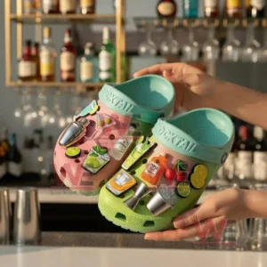 Hands lifting pink and green cocktail themed clogs in front of a bar filled with bottles!