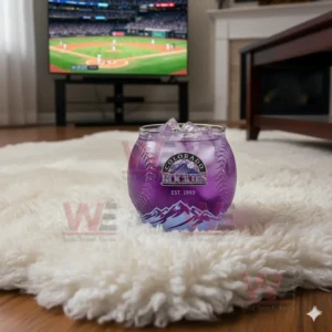 Colorado Rockies whiskey glass with purple drink and ice, sitting on a rug with a baseball game on TV in the background.