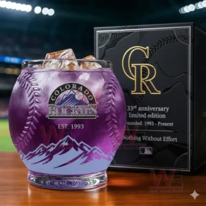 Colorado Rockies whiskey glass with ice and commemorative 33rd anniversary box, displayed in front of a baseball field.