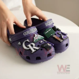 A person holding purple Colorado Rockies Crocs with baseball-themed charms attached.