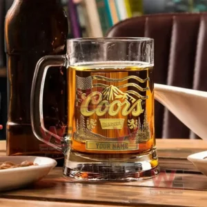 Alt text: Custom Coors Banquet beer mug with etched design, placed on a table with snacks and a beer bottle.