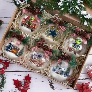 A gift box holding six Dallas Cowboys themed Christmas ornaments surrounded by greenery and ribbon.