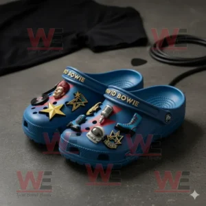 Blue Crocs with David Bowie themed charms including stars, microphone, boot, and space elements placed on a dark textured floor!
