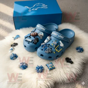 Blue Crocs with Detroit Lions logo and themed charms placed next to matching blue packaging on a soft rug!