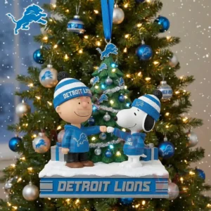 A Christmas ornament showing Snoopy and a boy in Detroit Lions gear fist bumping beside a decorated tree on a snowy platform!```