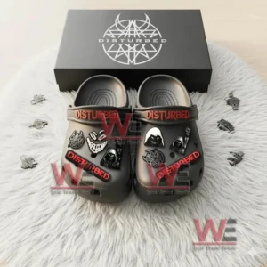 Black Disturbed Crocs with red logo and themed charms displayed on a white rug in front of a branded box.