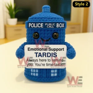 A blue crochet police box doll with a smiling face holding an encouraging message sign on a bright indoor table!