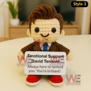 A crochet doll with brown hair and a friendly smile wearing a brown suit and red shoes holding a supportive message sign!