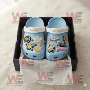 Light blue Elvis Presley Crocs with gold and black charms inside an open box on a fluffy surface!
