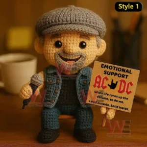 Crochet doll wearing denim clothes and gray cap holding a microphone and sign supporting AC DC on a wooden surface.