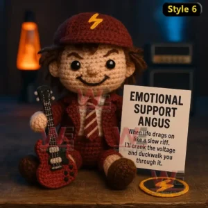 Emotional Support AC/DC Rock Band Doll 9 Crochet doll in red uniform holding guitar and AC DC support sign sitting on a wooden table.