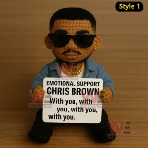 Crochet doll wearing blue jacket and sunglasses holding a sign supporting Chris Brown on wooden surface.