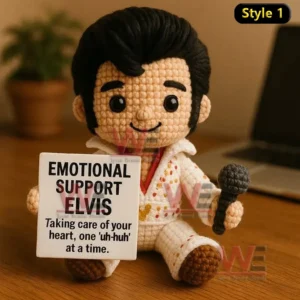 Crochet doll in white jumpsuit holding microphone and Emotional Support Elvis sign on a wooden table.