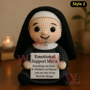 Crochet doll dressed as nun holding Emotional Support Maria sign on wooden surface with candle in background.