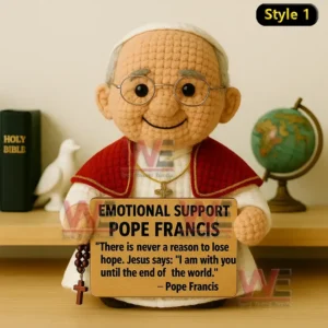 Crochet doll of pope wearing red cape and glasses holding Emotional Support Pope Francis sign with holy items in background.