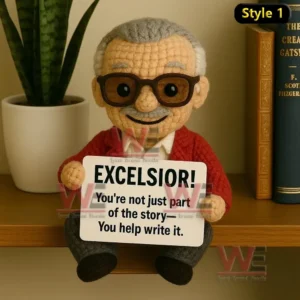 Crochet doll with gray hair red sweater and glasses holding Excelsior sign sitting on wooden shelf.