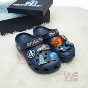 Blue Crocs decorated with Fantastic Four logos and superhero charms such as fire, metal fist, and futuristic gadgets shown on a fluffy white background beside the original box!