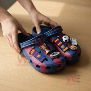 FC Barcelona themed clogs with various charms including a trophy a small football and club icons held by two hands on a wooden table.