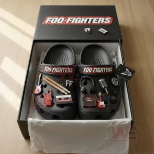 Black Crocs adorned with Foo Fighters themed charms such as drumsticks and amplifiers placed inside their branded box under soft daylight!
