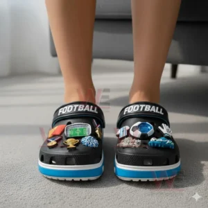 FOOTBALL PREMIUM Crocs Crocband CLOGS WITH CHARMS 5 A person standing indoors wearing black clogs adorned with various football themed charms!