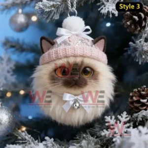 A cream cat ornament with a pink knit hat and white bow hanging on a Christmas tree!