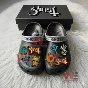Black Ghost Crocs with colorful band themed charms displayed in front of a branded box on a white rug.