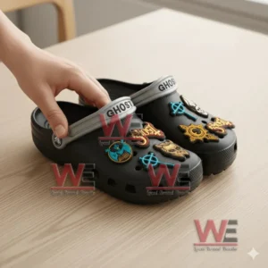 Close up of Ghost Crocs with gray straps and colorful charms being held by hand on a wooden surface.