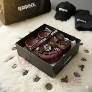 Maroon Crocs decorated with Godsmack logos and gothic charms like skull, dagger, and flame placed in their official packaging surrounded by matching accessories on a white rug!