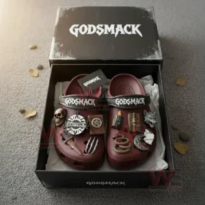 Maroon Crocs decorated with Godsmack symbols and gothic style metal charms placed inside their branded box on a gray textured floor with soft sunlight!