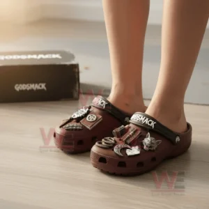 Dark red Crocs with Godsmack branding and metallic decorative charms shown on feet in a warmly lit indoor scene!